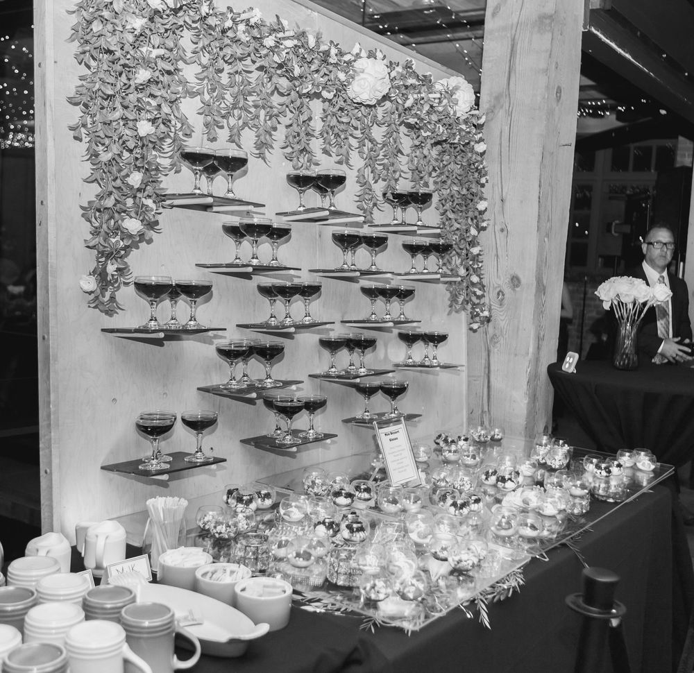 Black and white banquet room setup with elegant wine glass displays and decorative floral arrangements along a wall.