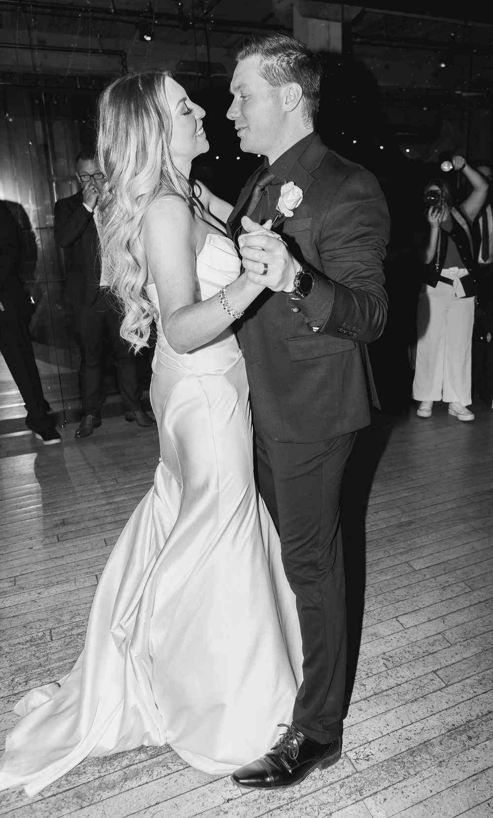 A couple shares their first dance in formal wedding attire on a rustic wooden dance floor.