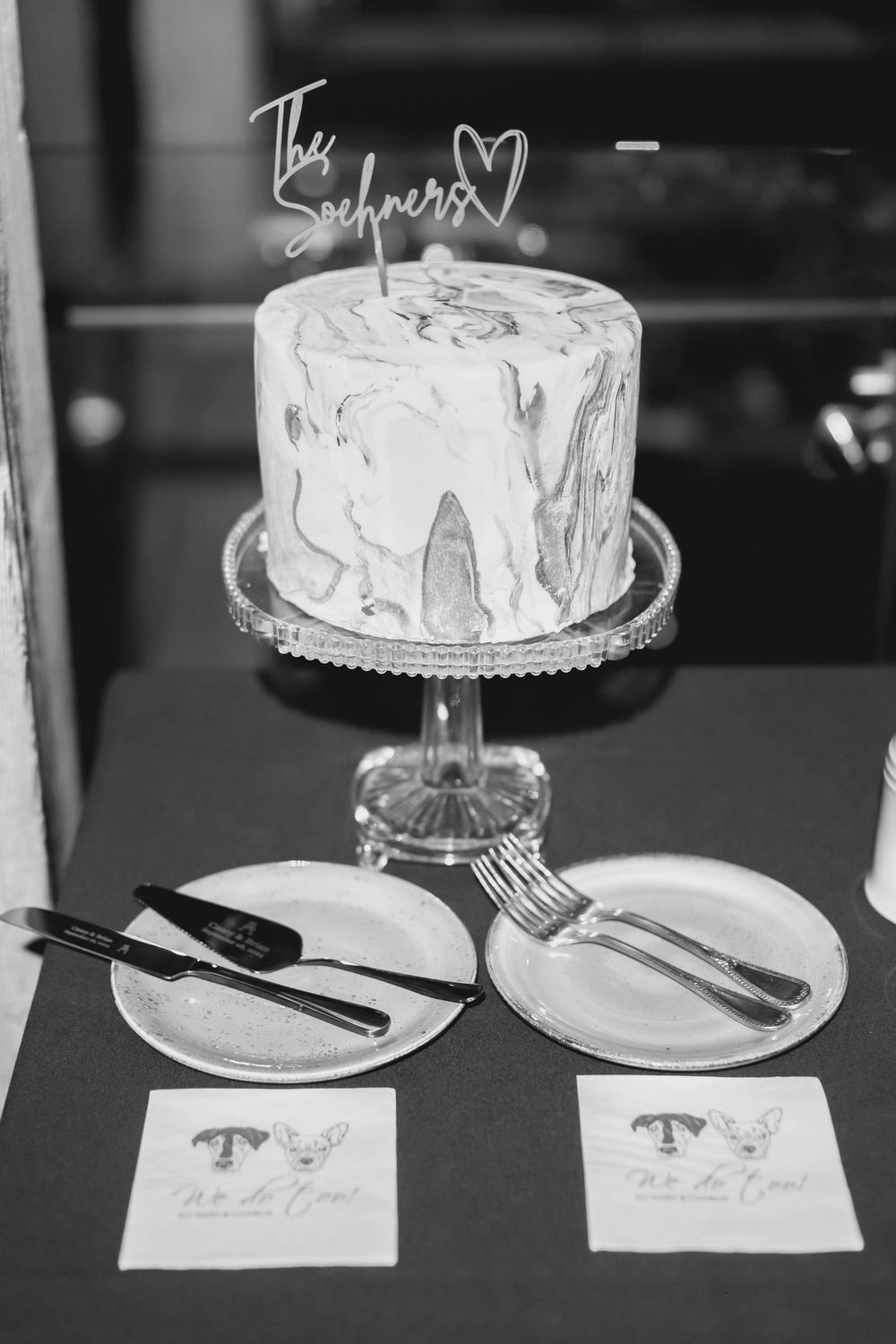 A marble-effect wedding cake displayed on a crystal cake stand with place settings and name cards below.