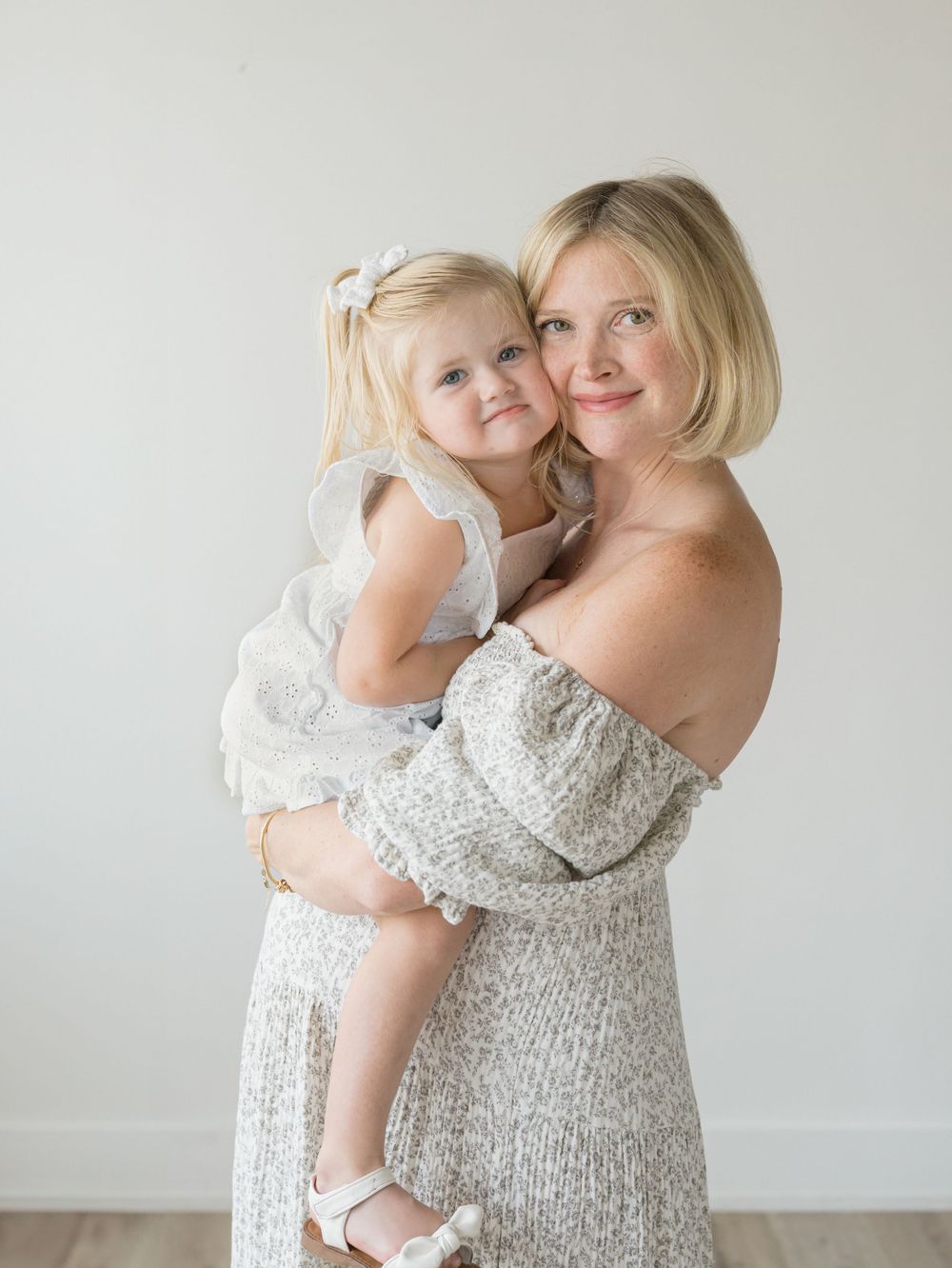 Mother cheek to cheek with big sister in a studio maternity session.