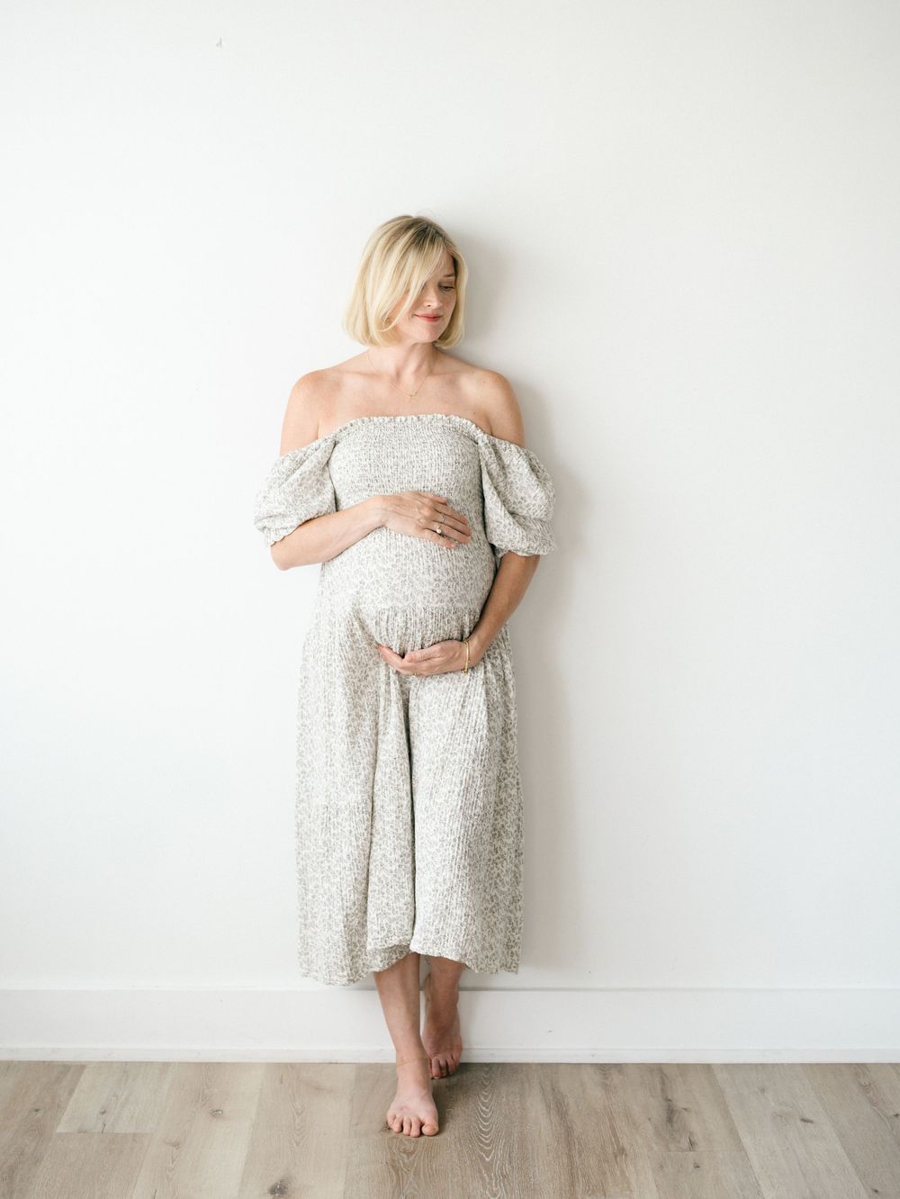 Elegant studio maternity portrait of expecting mother with soft window light and neutral backdrop.