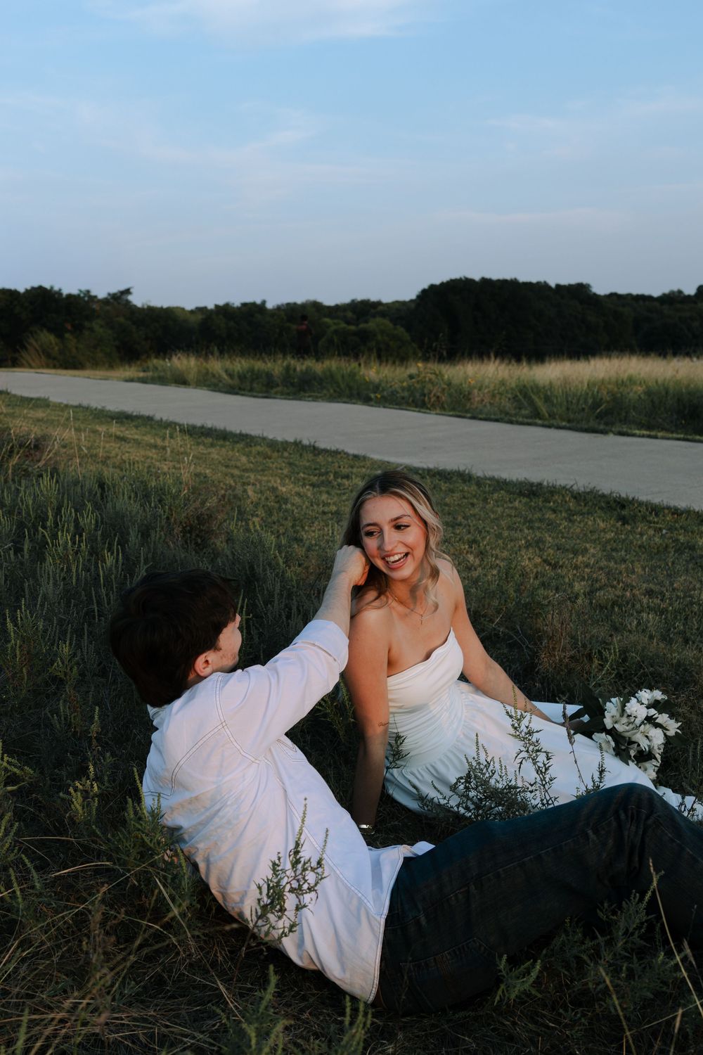 A romantic photoshoot in a grassy meadow with a couple in formal white and black attire.