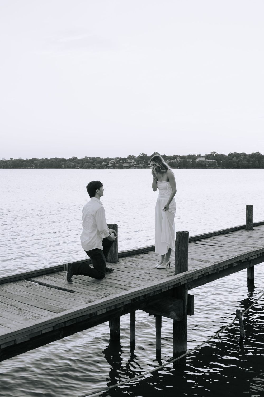 A black and white photo sequence shows a romantic proposal moment unfolding on a wooden dock over calm waters.