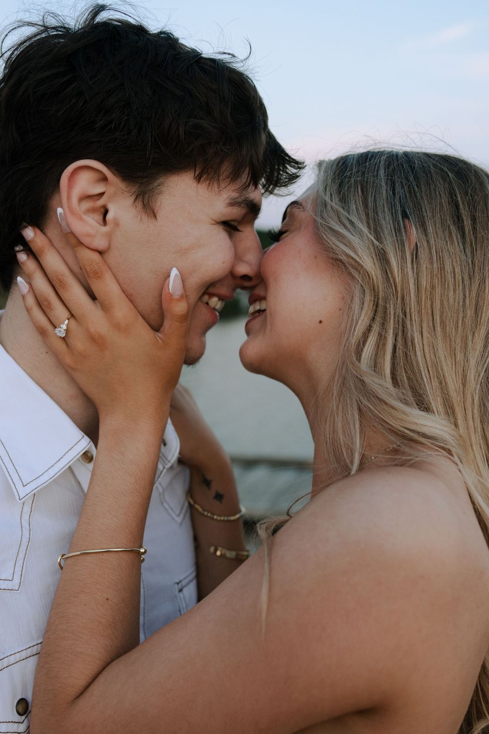A romantic couple shares an intimate moment at sunset, embracing and smiling while gazing at each other.