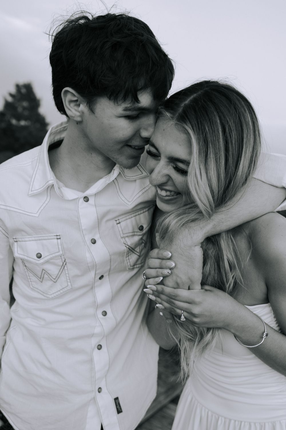 A couple in white outfits shares playful laughter and embraces in black and white photography.