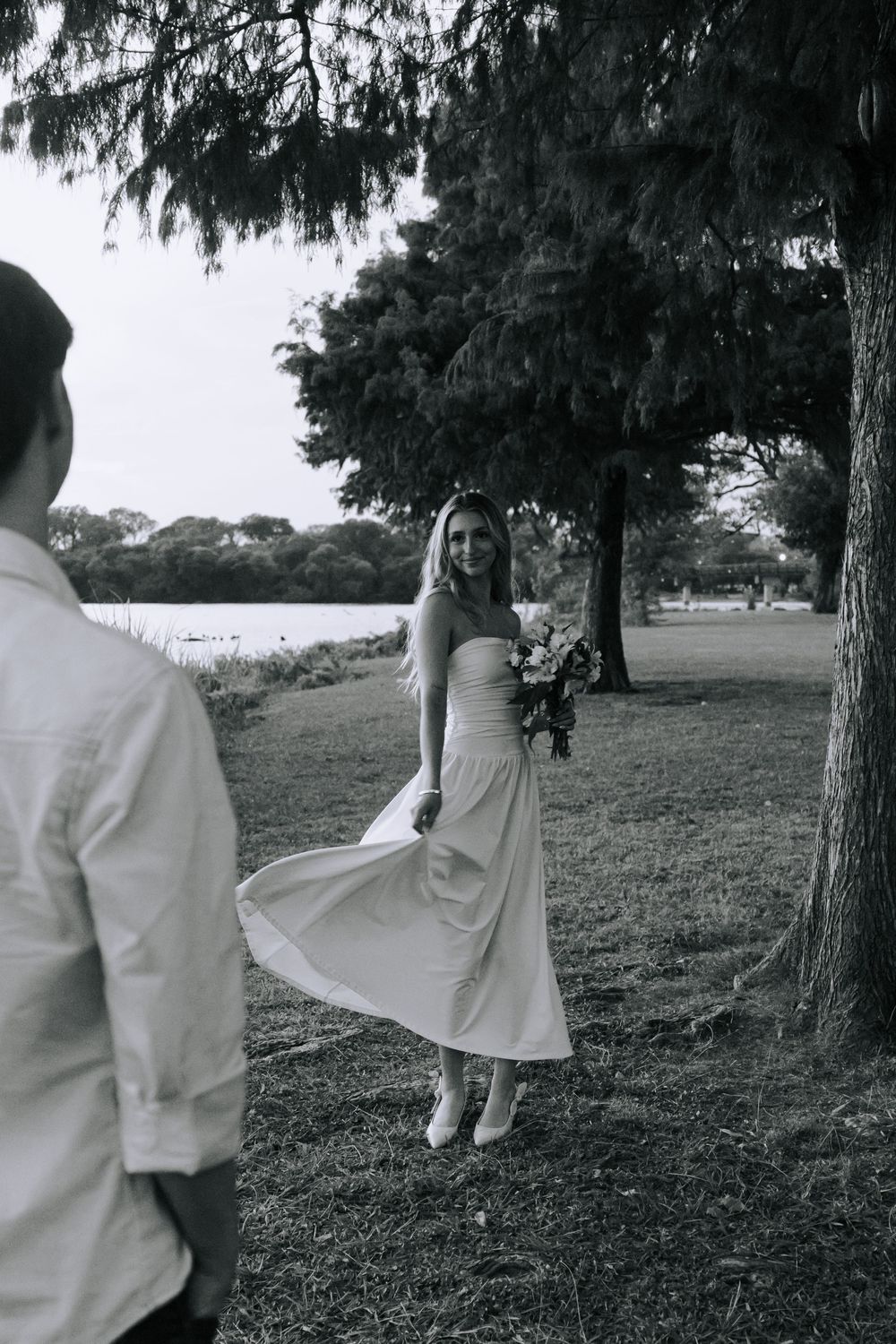 A person in white clothing swings playfully on a tree branch in a serene outdoor setting.