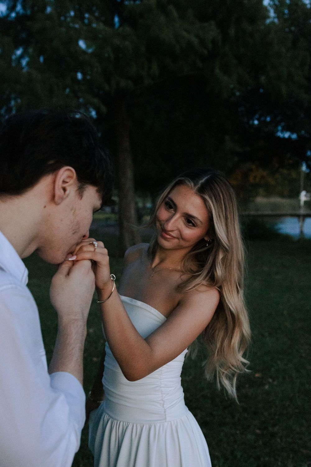 Intimate moment between couple wearing white as they dance together in an outdoor setting at dusk.