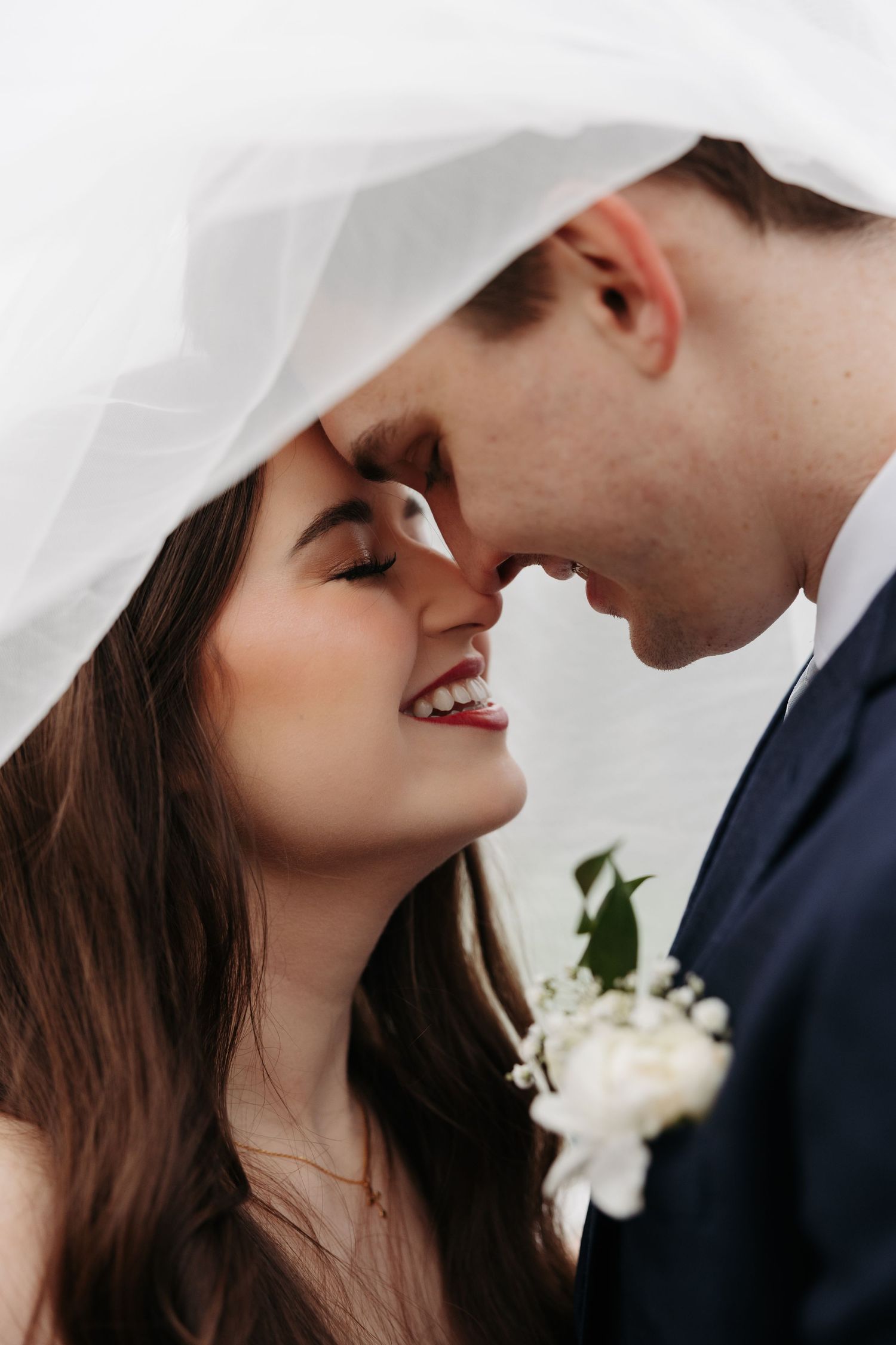 A couple on their wedding day hold hands while standing around a corner of a white building with lanterns.