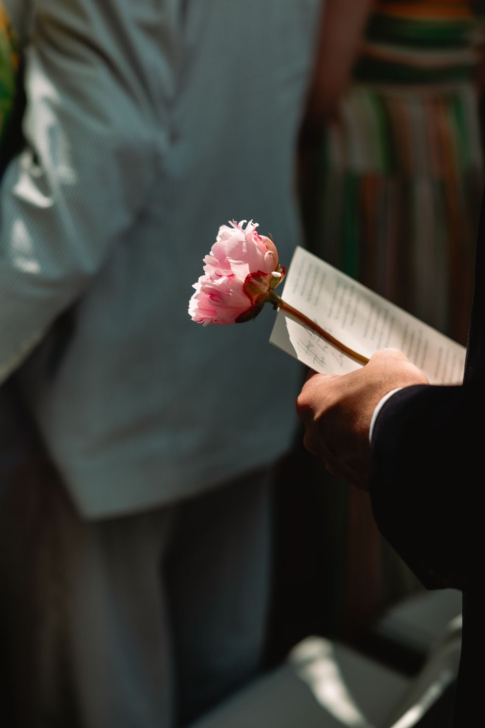 Guest holding pink peony flower and ceremony program during an elegant wedding service.
