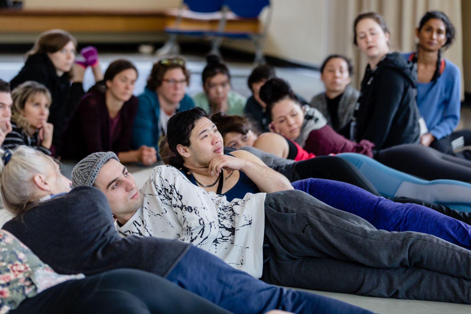 Group of people lying down and relaxing during a workshop or meditation session in a bright indoor space.