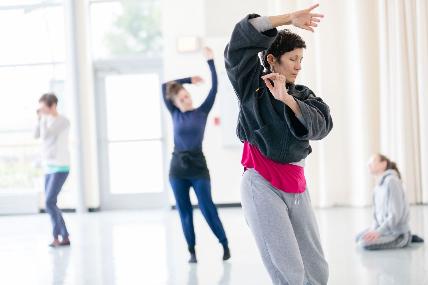 Dancers practicing in a bright studio space wearing athletic wear move gracefully during a dance class.