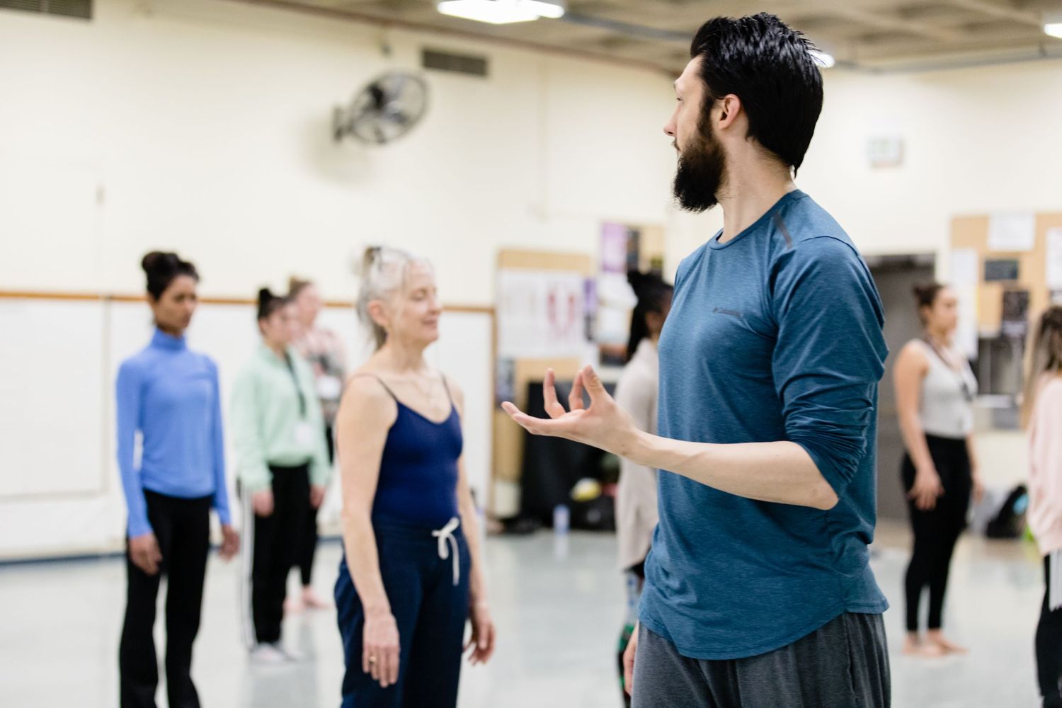 Dance instructor leads a group class in a studio space while demonstrating movement techniques.