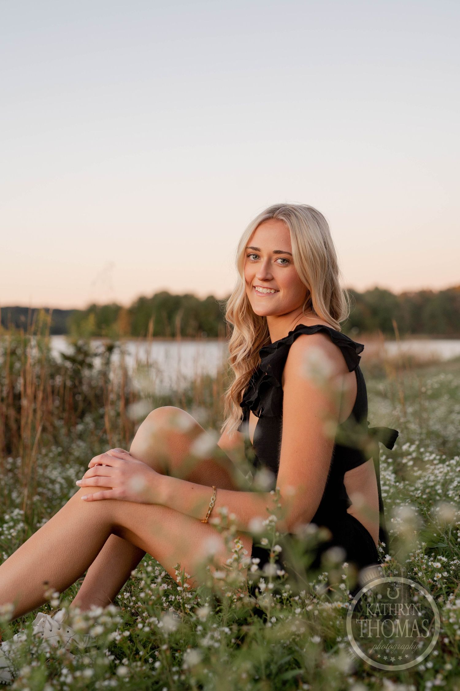Natural outdoor portrait amid blooming wildflowers with lake and trees in background.