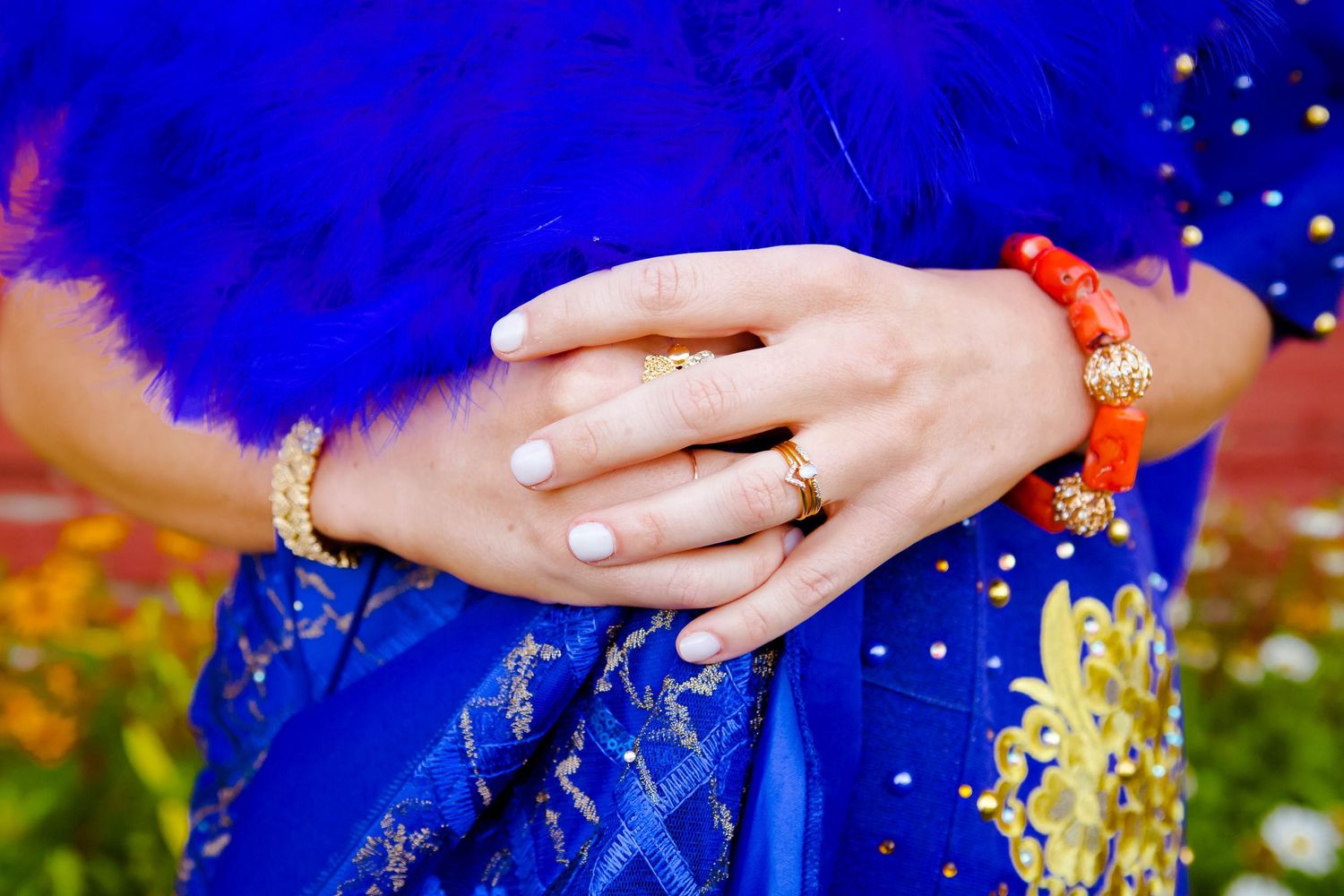 Hand with white nail polish and silver bracelet against vivid blue fabric with red and gold details.