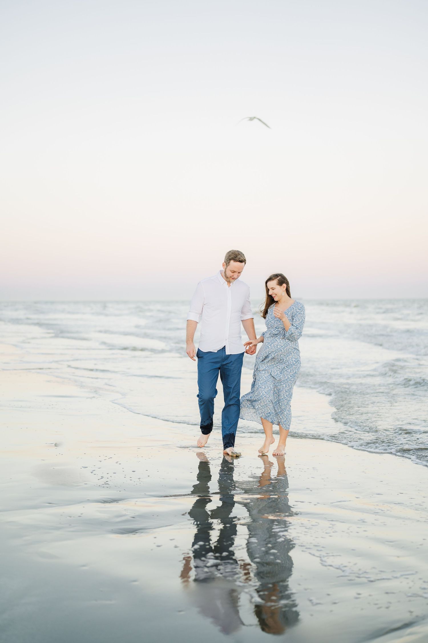 Couple strolling along beach at sunset creating reflections in wet sand.