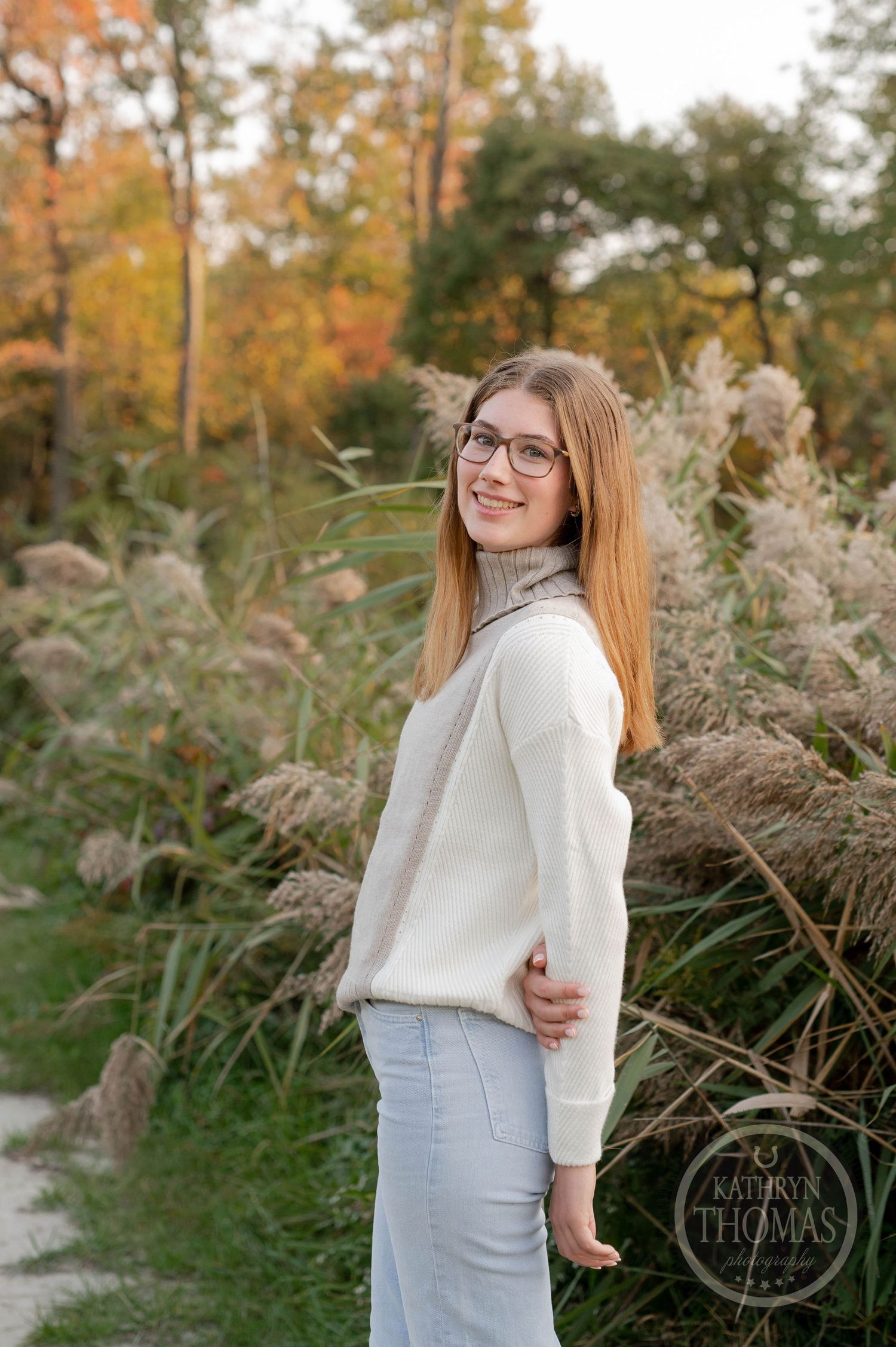 Natural outdoor photo showing someone in light-colored sweater posing among tall grasses.