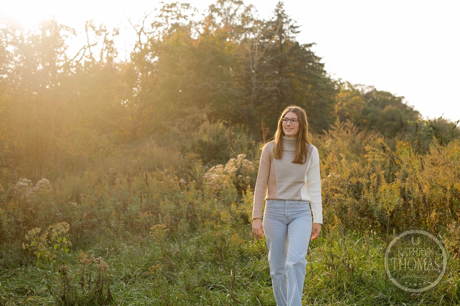 Natural outdoor photo of someone walking through a field at sunset wearing casual attire.