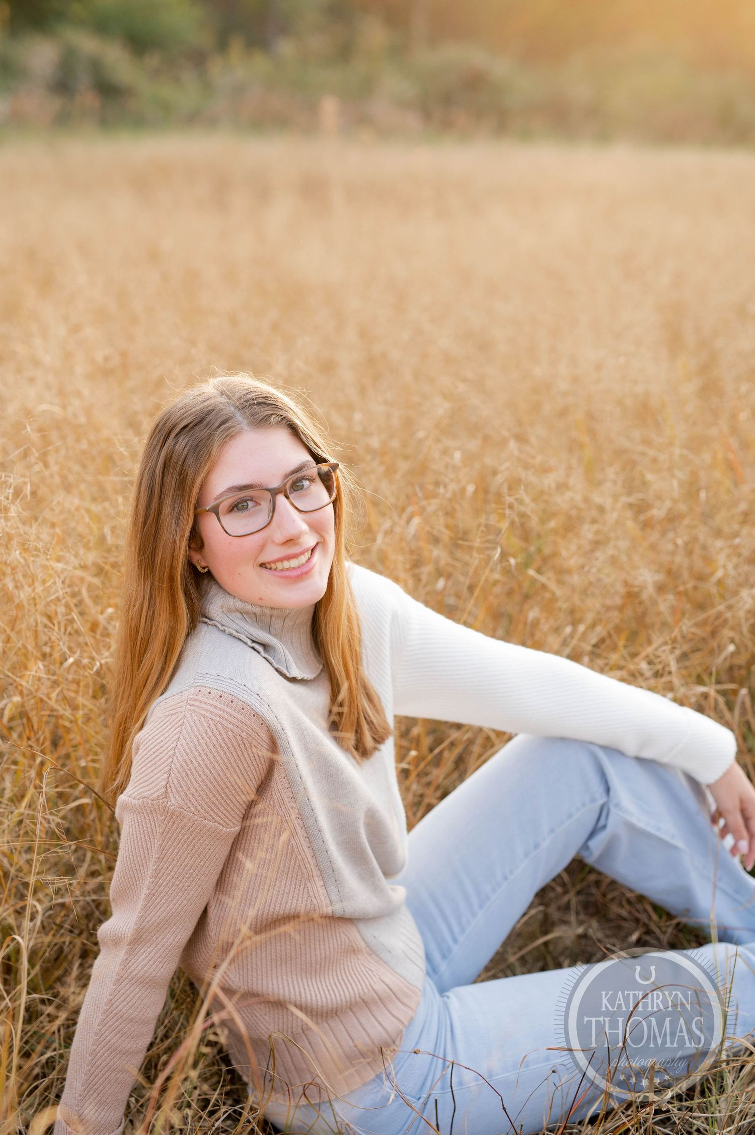 Relaxed autumn portrait sitting in golden field wearing layered sweaters at sunset.