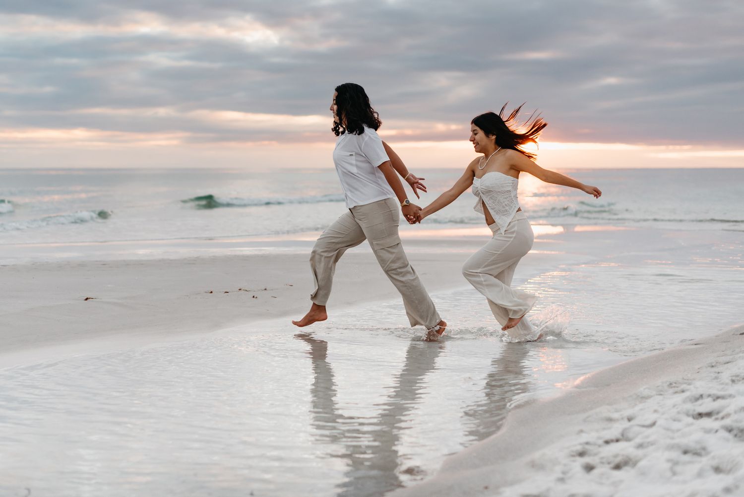 Two people dance playfully in the shallow ocean waves at sunset.