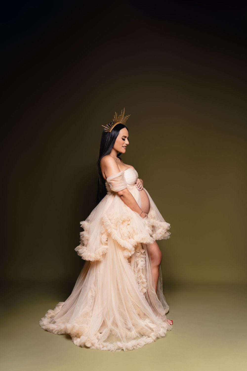 Maternity portrait of woman in flowing peach gown against dark background.