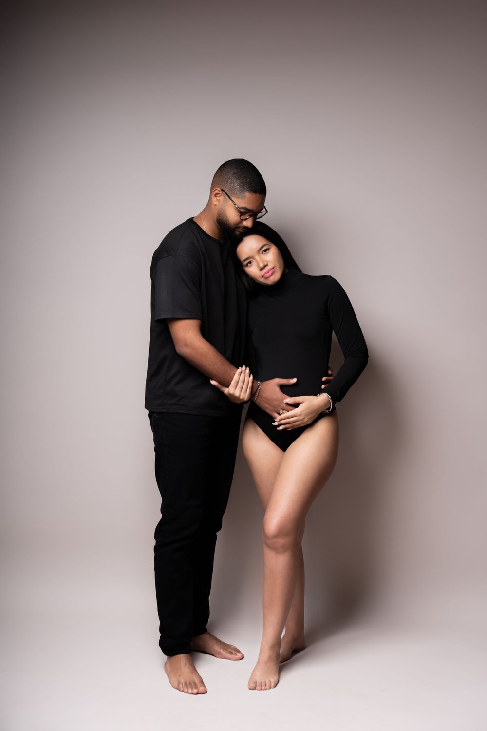 Intimate maternity portrait of couple in black attire against neutral background.