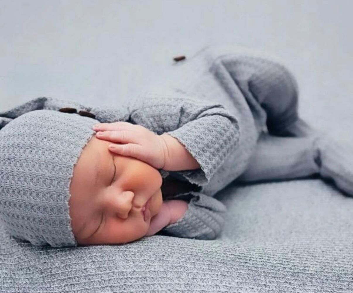 Peaceful newborn sleeping on textured gray blanket wearing cozy knit outfit.