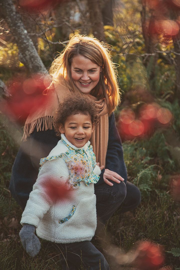 Mamma och dotter som leker i skogen bland rönnbärsbuskar. Varmt ljus, spontan och lekfull stämning.