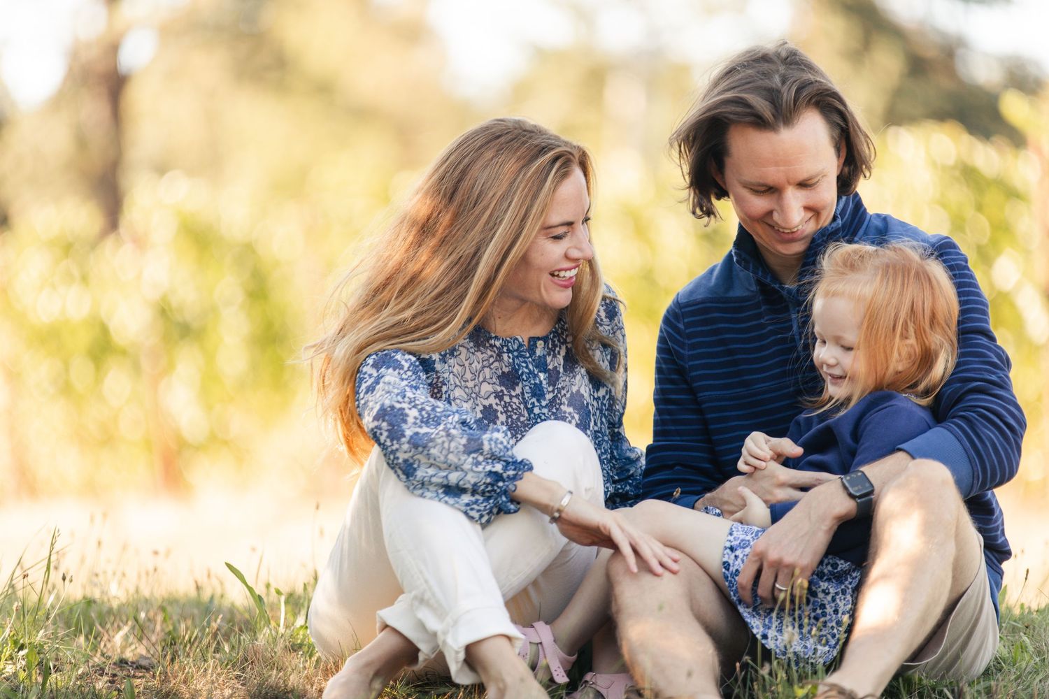 A family sits together in a sunlit field during golden hour enjoying a tender moment with their child and dog.