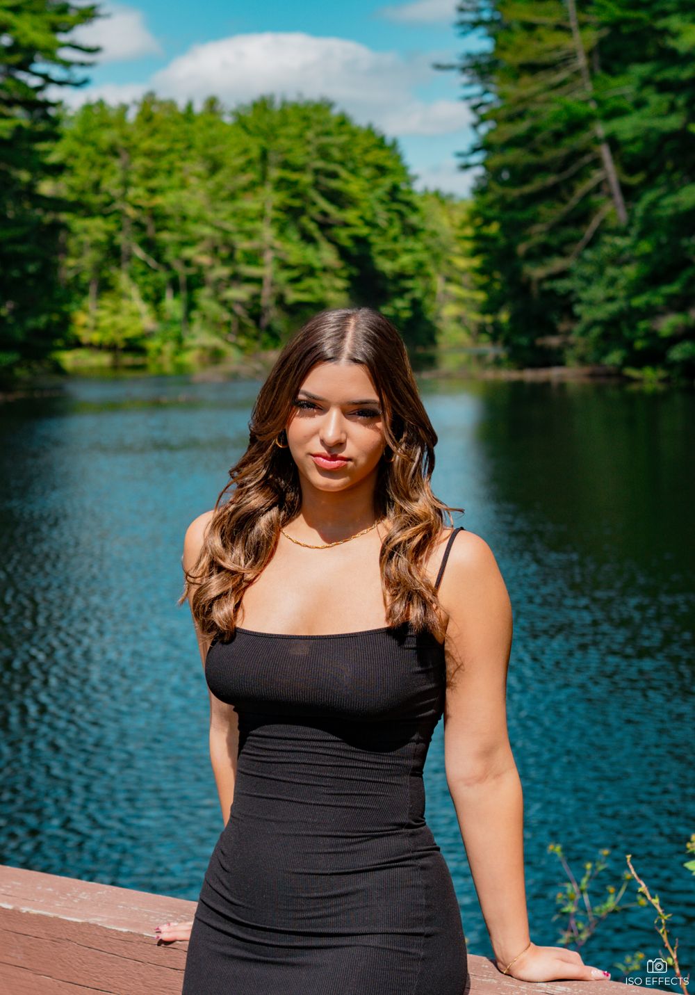 A lakeside photo taken on a wooden deck with evergreen trees reflected in the calm water.