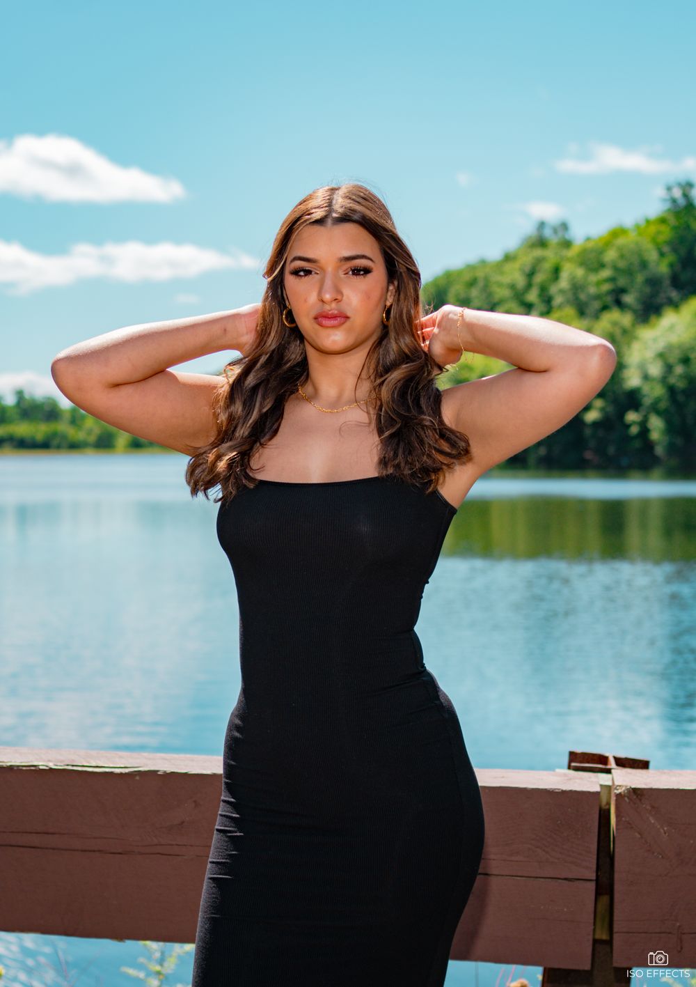 Summer fashion photoshoot on a wooden deck overlooking a tranquil lake and forest.