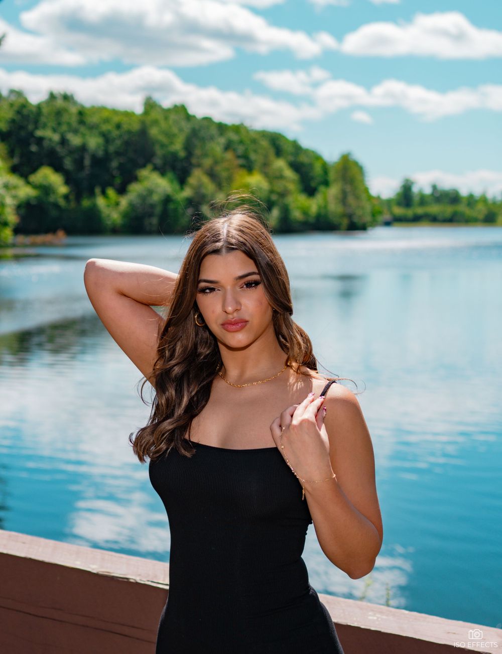 Outdoor portrait featuring a black dress against a scenic lake backdrop on a sunny day.