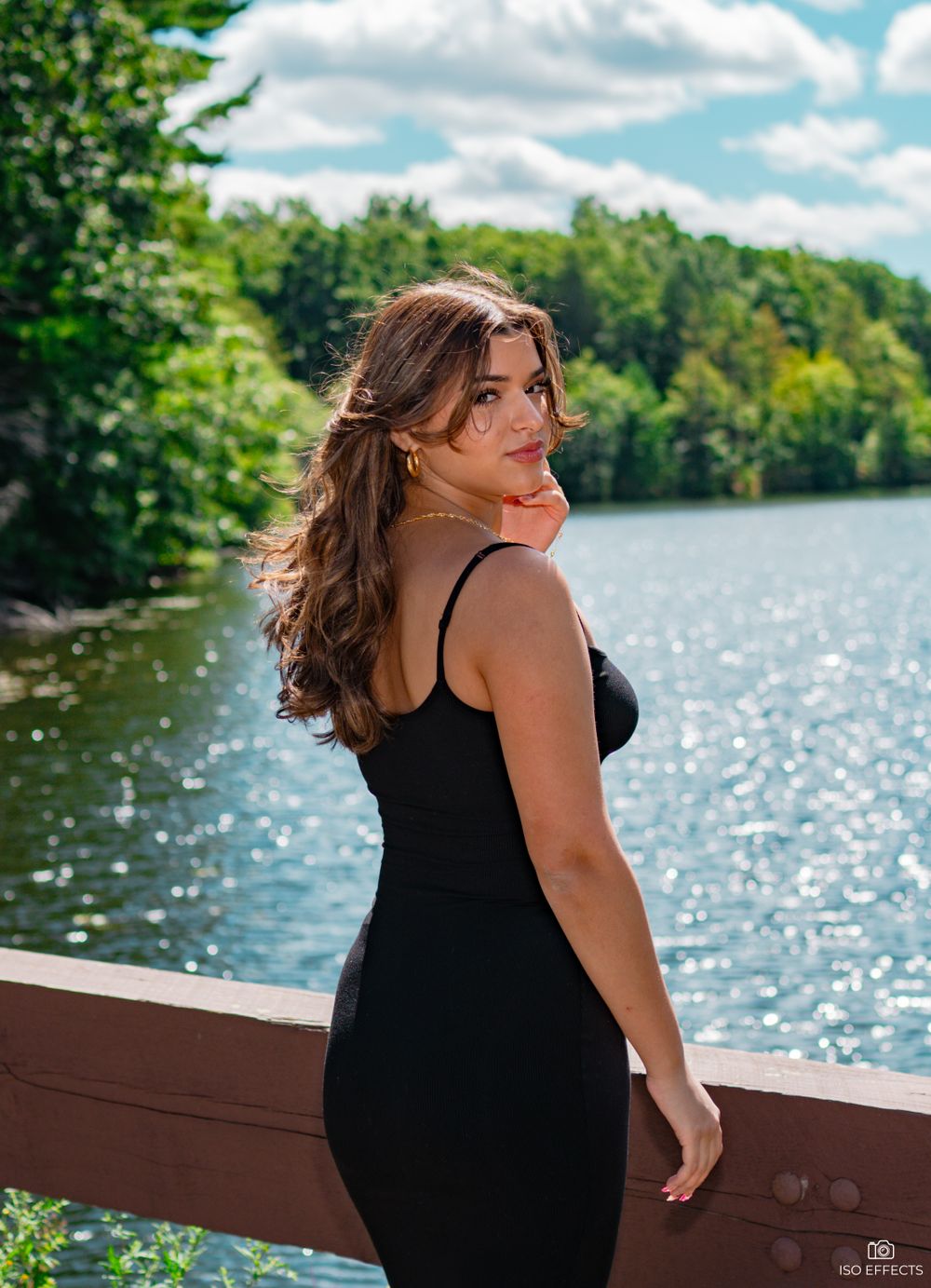 Candid lakeside portrait with sparkling water and forest scenery in the background.