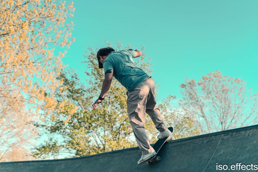 Skateboarder performing trick on ramp against turquoise sky and autumn trees.