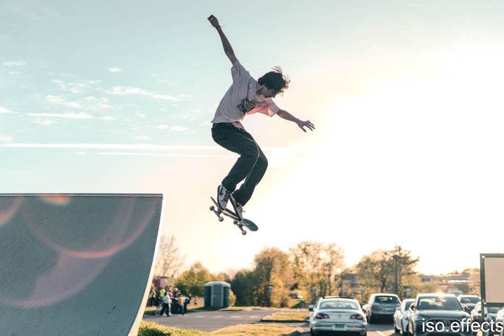 Silhouette of skateboarder performing aerial trick at sunset with cars in background.