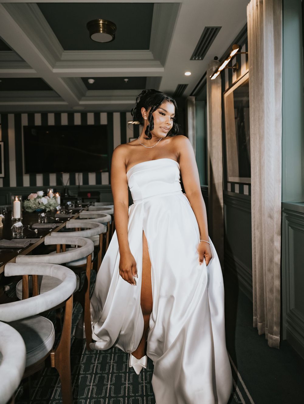 Person in white strapless wedding gown poses elegantly inside an upscale restaurant with striped walls and curved seating.