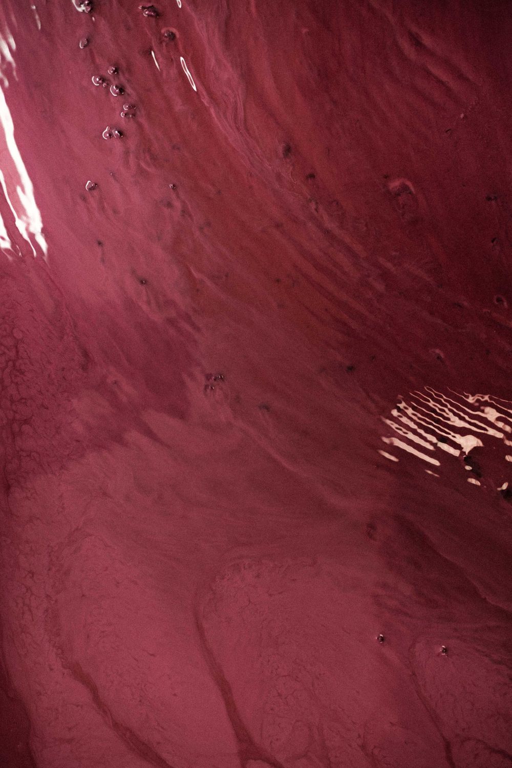 Deep burgundy red wine liquid surface with ripples and bubbles.