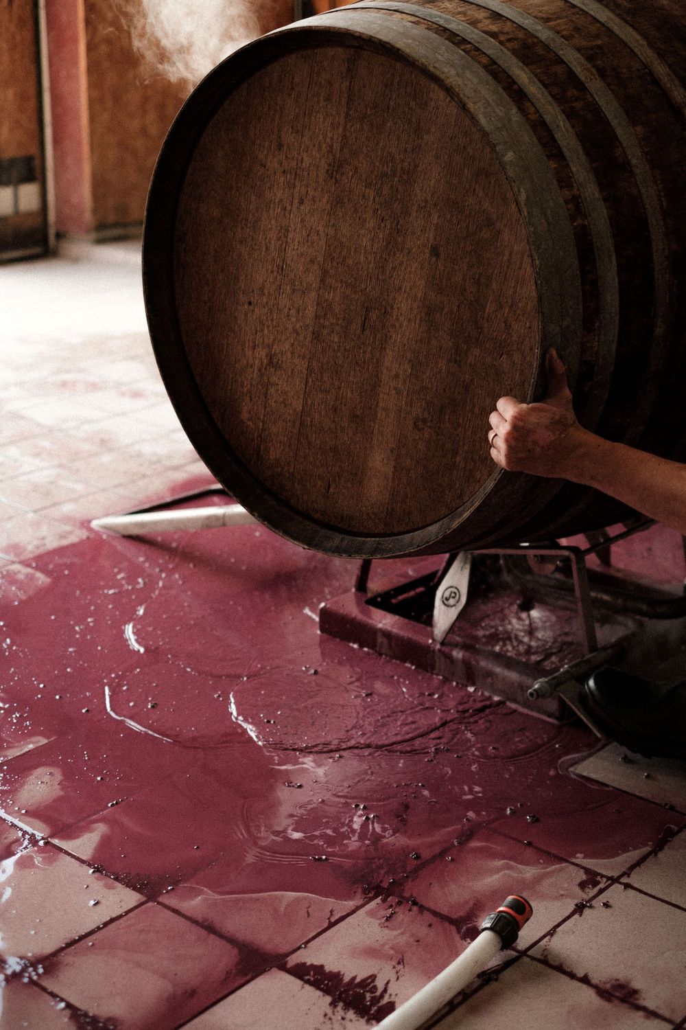 Traditional wooden wine barrel on tiled floor with liquid spills.