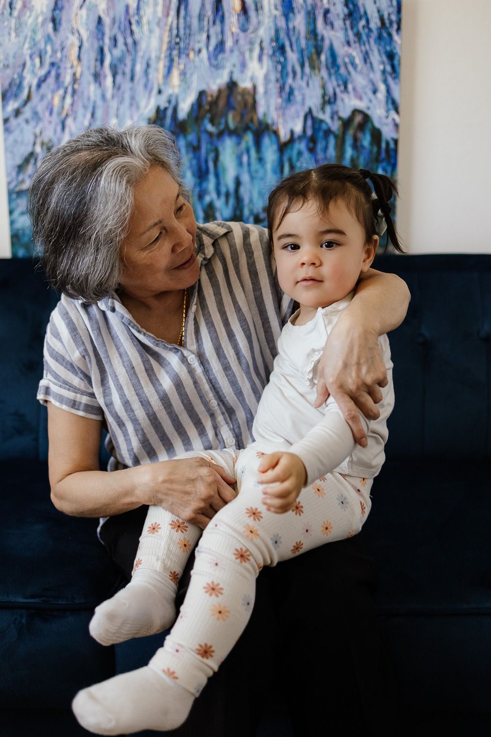 Toddler girl sits on her grandmother's lap during her family's newborn lifestyle photo session in San Jose