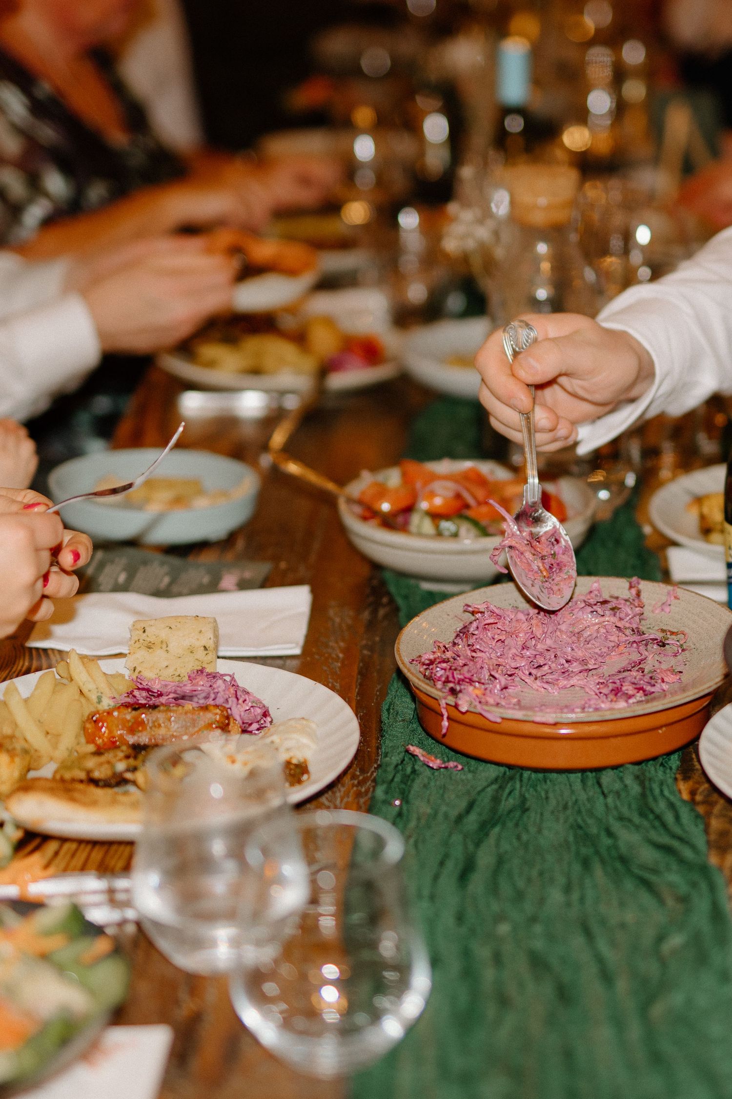 People enjoy a dinner gathering with vibrant pink beet dip and appetizers served on a rustic wooden table with green linens.