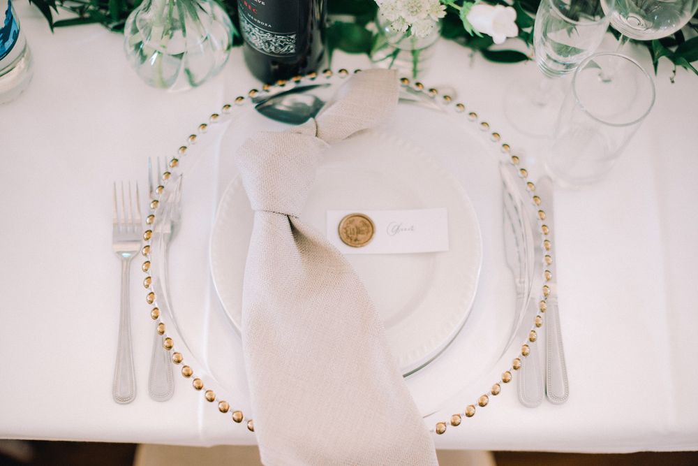 Elegant white place setting with gold beaded charger plate and napkin with wax seal on white tablecloth at The Halifax Club