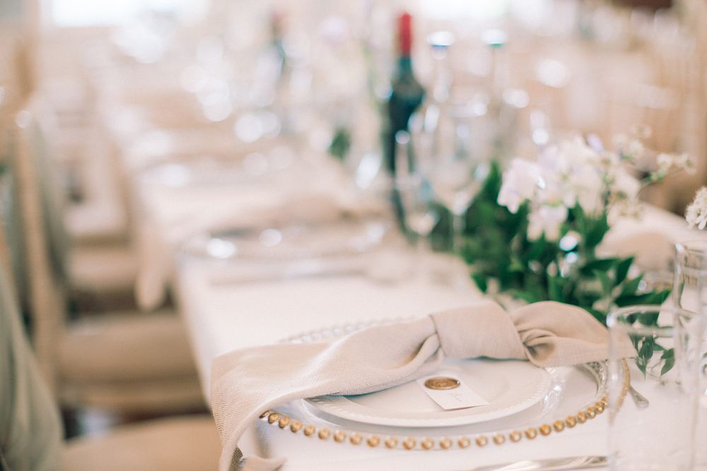 An elegant white table setting at a wedding reception with gold-rimmed plates and delicate floral centerpieces at The Halifax Club