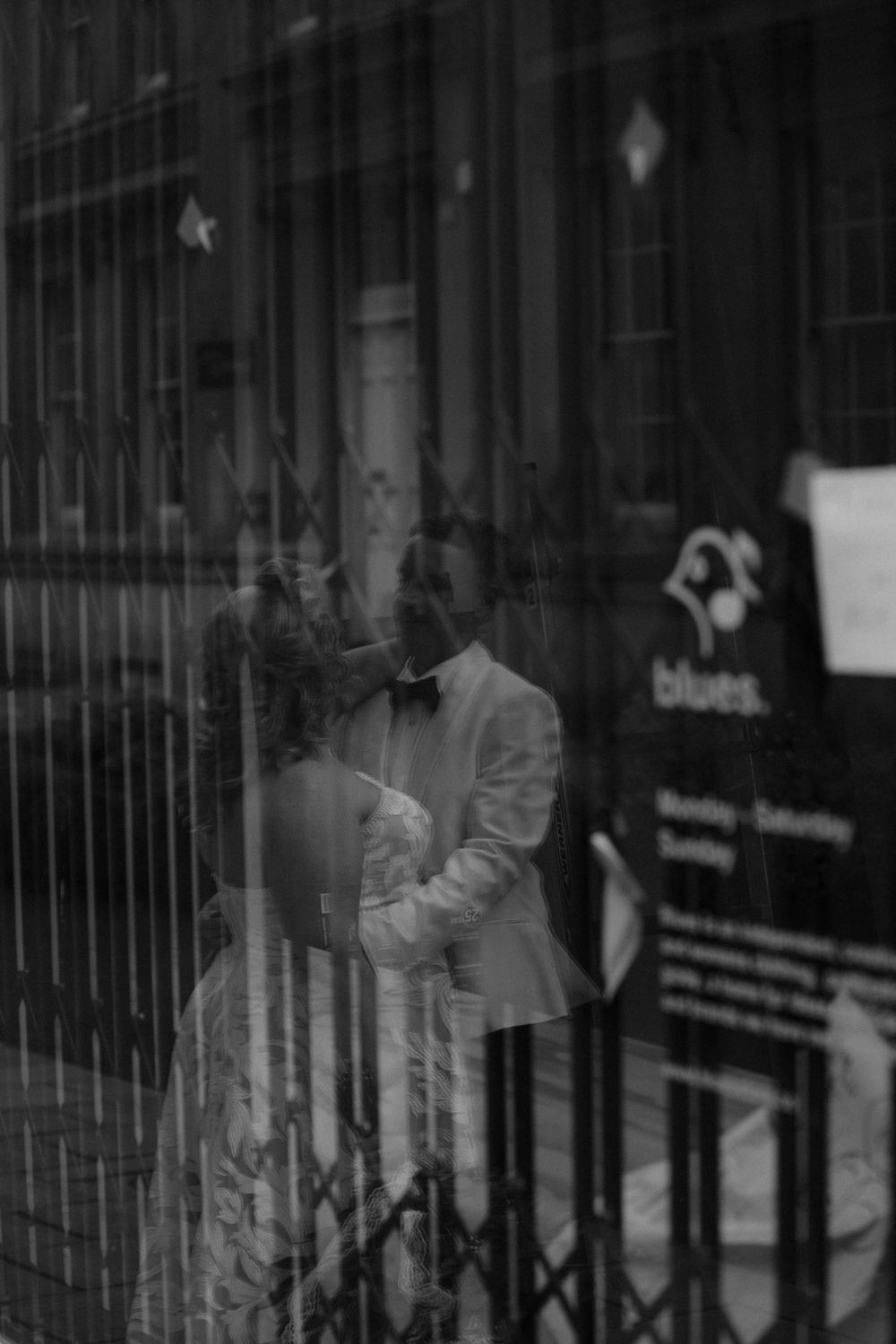 A black and white photograph showing a ghostly reflection in a storefront window with iron bars and signage downtown at The Halifax Club