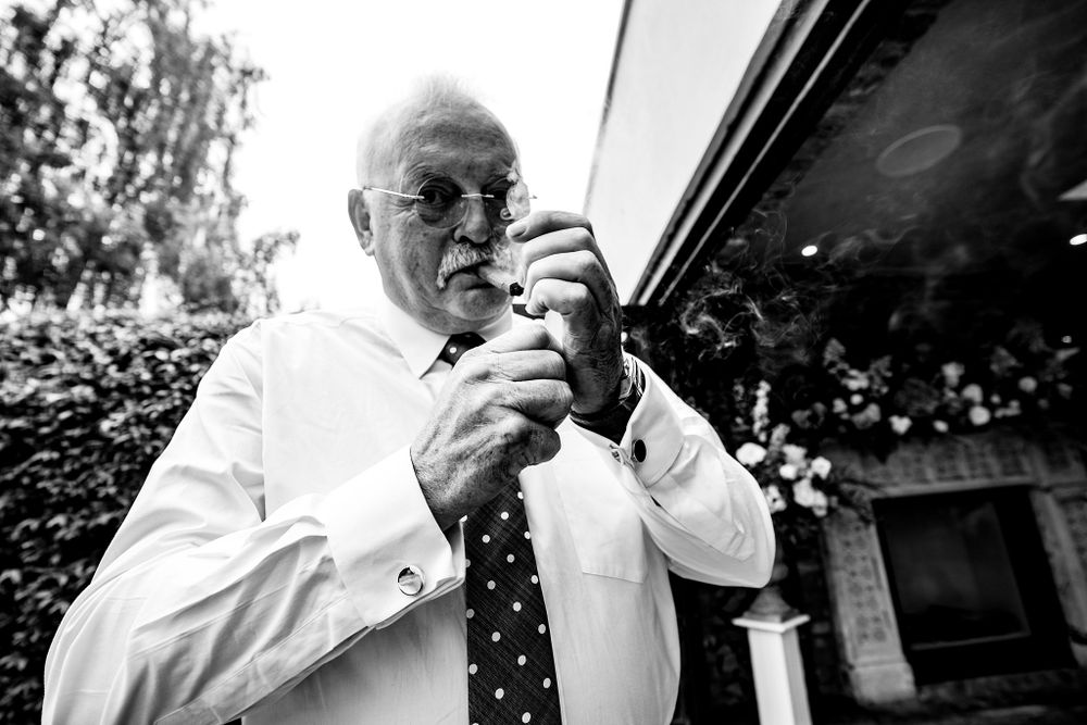 Black and white photo of person in formal attire lighting a cigar outdoors at The Halifax Club