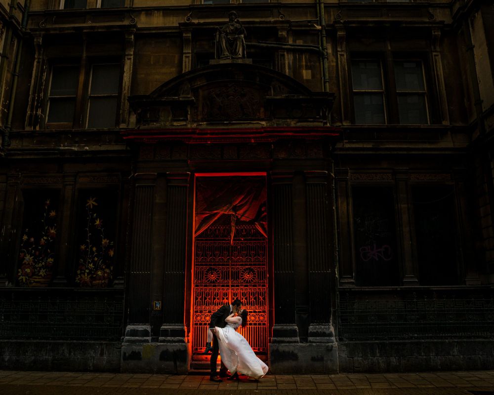 A white-clad figure stands before an ornate Gothic church doorway illuminated in dramatic red lighting at night at The Halifax Club