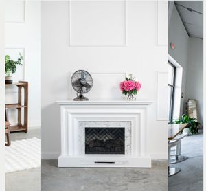 Clean white studio space with marble fireplace, potted plants and modern furniture arrangements.