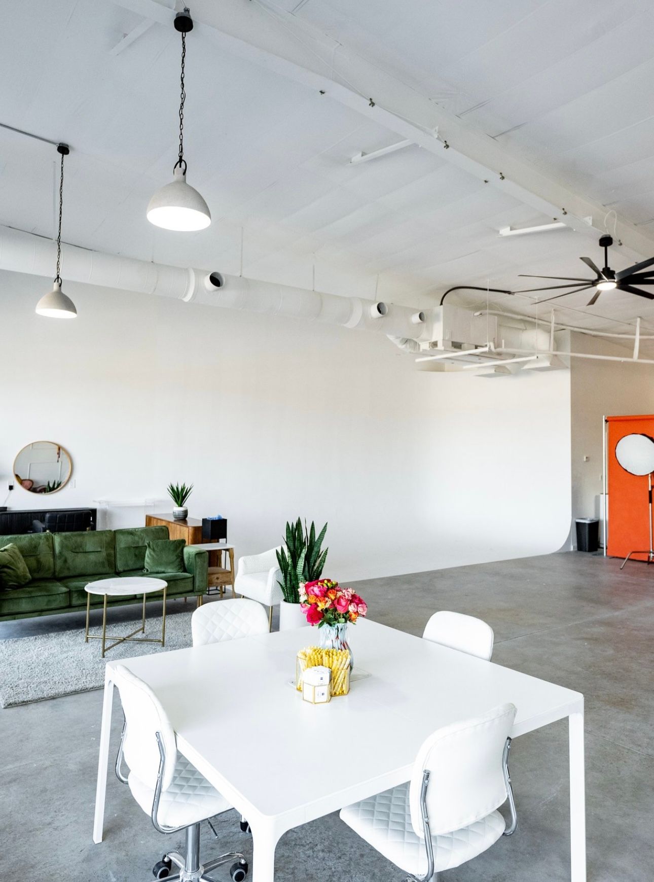Modern white studio space with minimalist furniture and high ceilings features white tables and chairs.