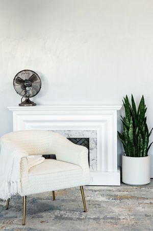 White modern fireplace with decorative plants and vintage-style fan in a bright interior setting.