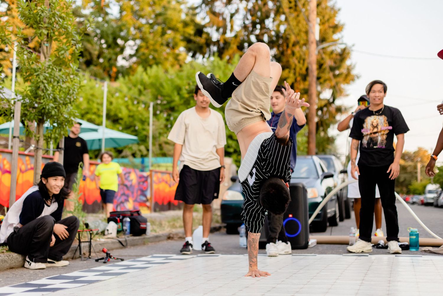 A breakdancer performs an athletic move on the street while others watch during an outdoor dance session.
