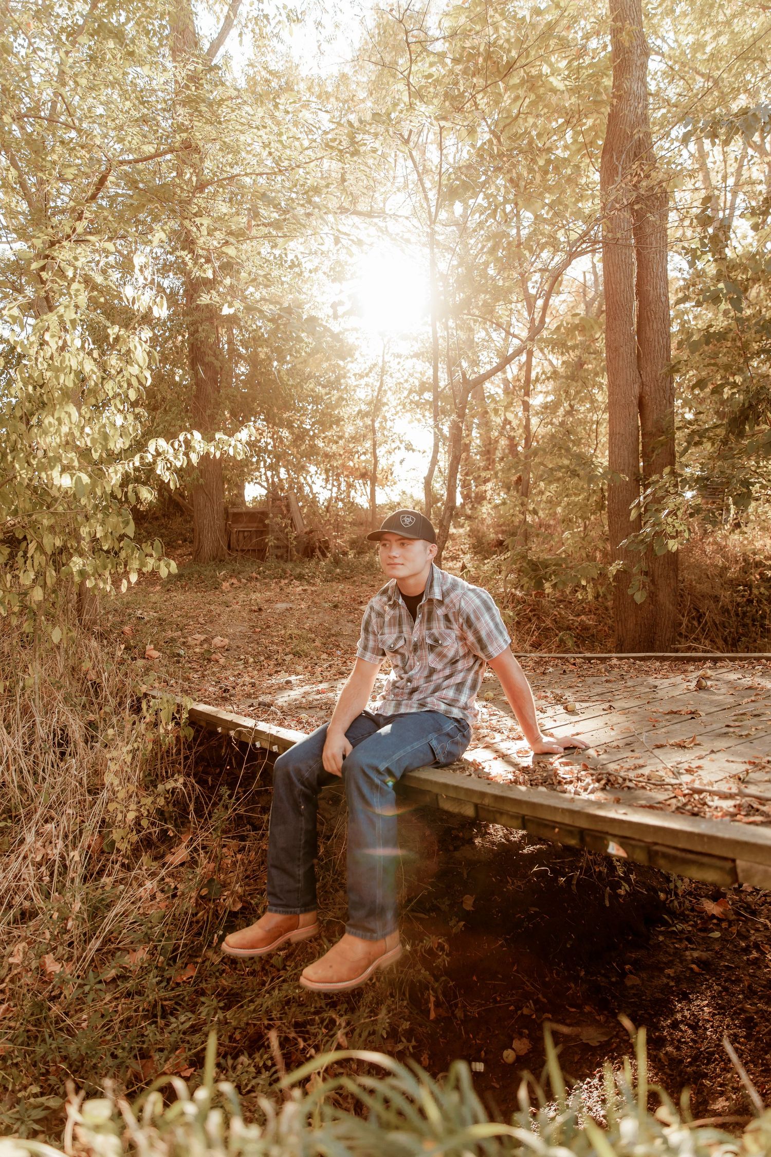 Sun flare illuminates a rustic autumn scene with someone sitting on a wooden platform in the woods.