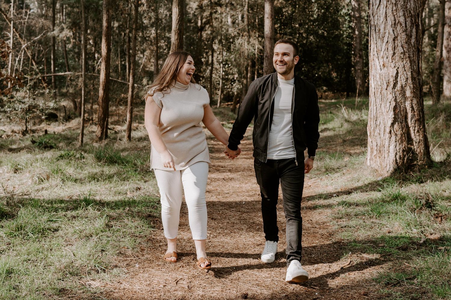 A couple are walking hand in hand in the woods at well next the sea, Norfolk. The lady is laughing and looking at her husband.